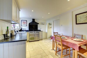 A kitchen with a central island, a dining table with a red and white checkered tablecloth, and a black range hood above the stove. - 2 Bed in Orford (oc-sflis) (Orford)