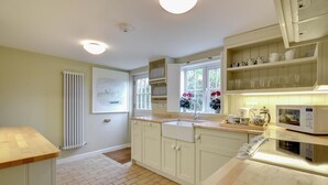 A kitchen with white cabinets, a sink, a window with flowers, and a microwave. - 2 Bed in Iken (oc-sfboo) (Iken)