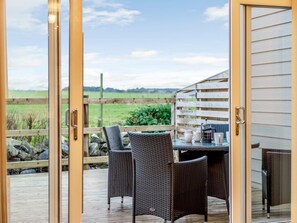 A glass door leading to an outdoor patio with wicker furniture and a coffee table, overlooking a grassy field. - 2 Bed in Alnwick (oc-80494) (Newton-by-the-Sea)