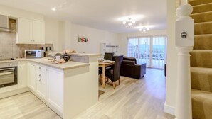 A modern kitchen with white cabinets, a microwave, and a dining area with a table and chairs. - 2 Bed in Alnwick (oc-80494) (Newton-by-the-Sea)