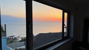 Una stanza con un'ampia finestra che si affaccia su una vista costiera al tramonto.