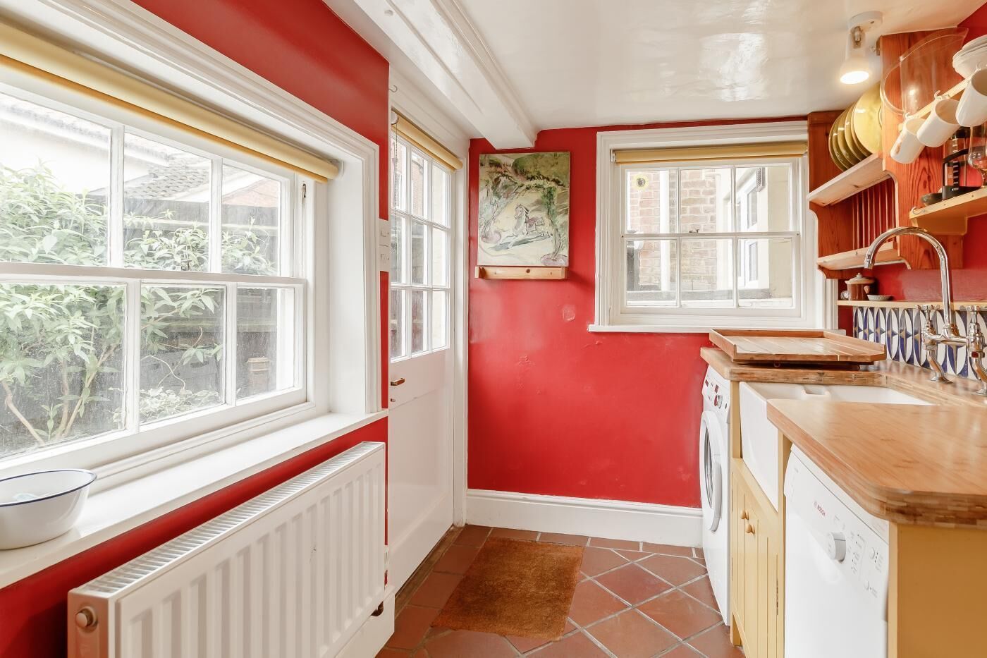 Una cocina pequeña con paredes rojas, detalles blancos y una ventana con vistas a la vegetación.