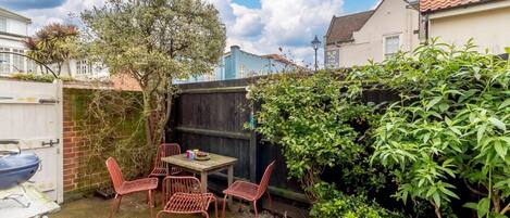 A patio with a table and chairs, surrounded by a wooden fence and greenery.