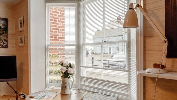 Et hyggeligt værelse med et stort vindue, et lille bord med en blomstervase, en lampe og et fjernsyn.