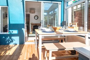 Ein heller Raum mit Holzboden, einem Tisch mit Stühlen und Blick auf einen Ziegelkamin durch eine Glastür.