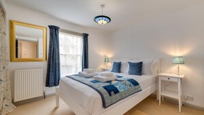 A neatly arranged bedroom with a large bed, a bedside table with a lamp, a radiator, and a window with curtains. - 2 Bed in Woodbridge (oc-48sc) (Woodbridge)