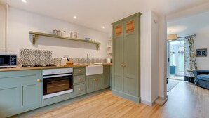 A modern kitchen with light green cabinets, a microwave, a stove, and a sink. There is a wooden countertop and a patterned backsplash. - 2 Bed in Woodbridge (oc-48sc) (Woodbridge)
