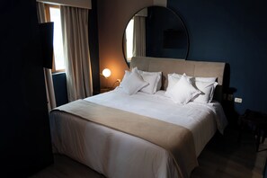 A neatly made bed with white linens and pillows, a round mirror on the wall, and a bedside lamp. - Olivar House Hotel (Lima)