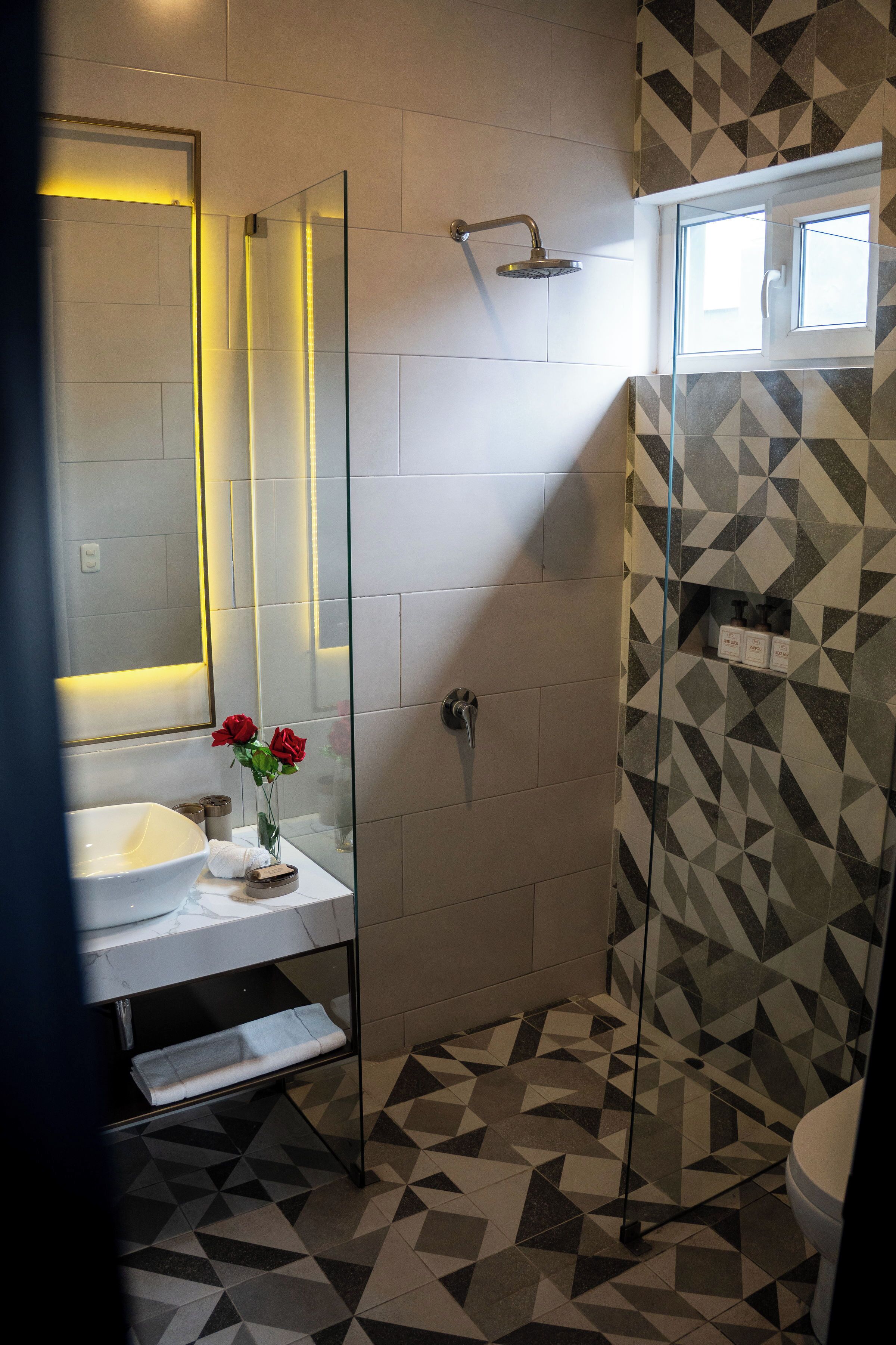 A modern bathroom with a glass shower enclosure, a white sink with a marble countertop, and a geometric patterned floor.