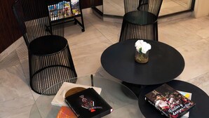 Una hall moderna con sedie nere, un tavolo rotondo con un vaso e una libreria con riviste.