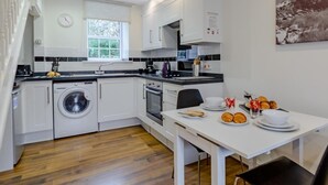 A modern kitchen with white cabinetry, a built-in washing machine, and a dining area with a table set for two. - 1 Bed in Alnwick (oc-80486) (Newton-by-the-Sea)