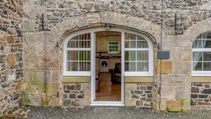 A stone building with a large arched doorway leading into a room with a wooden floor and a sofa. - 1 Bed in Alnwick (oc-80486) (Newton-by-the-Sea)