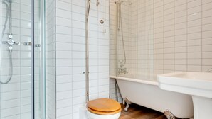 Une salle de bain dotée d’une douche à parois de verre, d’une baignoire sur pieds et de toilettes avec un abattant en bois.