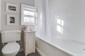 A bathroom with a toilet, a cabinet, a bathtub, and a window with blinds.