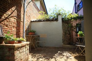 A small courtyard with brick walls, a white wall, and a stone wall. There are potted plants and a folding chair.