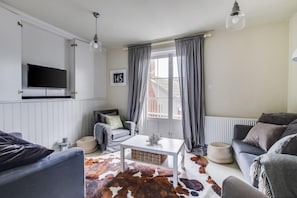 A living room with a TV, a sofa, a chair, a coffee table, and a cowhide rug.