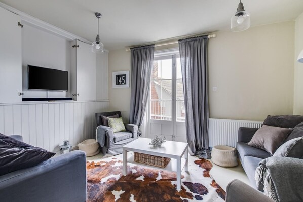 Un salon comprenant un téléviseur, un canapé, un fauteuil, une table basse et un tapis en peau de vache.