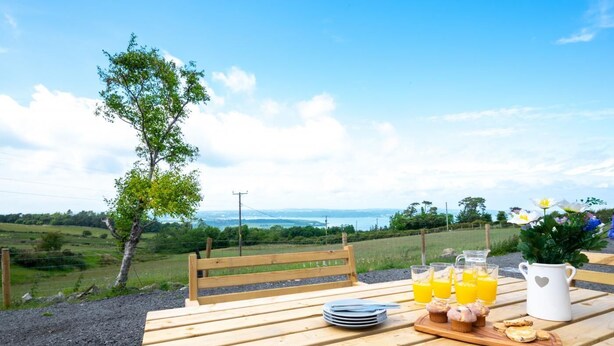 Une table en bois avec un banc, une carafe, des verres de jus d’orange et une assiette de nourriture.