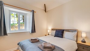 Un lit bien fait, avec une couverture bleue et deux serviettes pliées, une table de chevet avec une lampe et une fenêtre avec des rideaux.