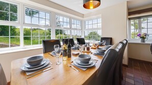 Un coin repas avec une table en bois dressée pour quatre personnes, de grandes fenêtres et un luminaire suspendu.