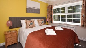 A bedroom with a bed, a nightstand, a window with curtains, and a chandelier. - 4 Bed in Alnwick (oc-80496) (Newton-by-the-Sea)
