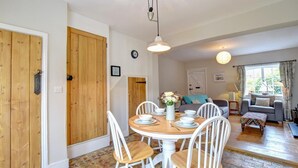 A dining area with a wooden table and chairs, a white vase with flowers, and a clock on the wall. - 2 Bed in Orford (oc-sflpo) (Orford)