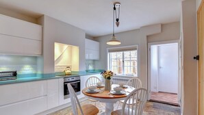 A modern kitchen with white cabinets, a built-in oven, and a dining area with a table set for four. - 2 Bed in Orford (oc-sflpo) (Orford)