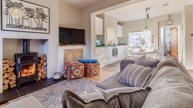 A living room with a fireplace, a sofa, a television, and a kitchen in the background. - 2 Bed in Orford (oc-sflpo) (Orford)