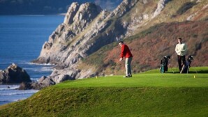 Een golfbaan met uitzicht op de oceaan en heuvelachtige rotsformaties.