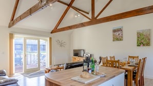 A spacious living area with a wooden ceiling, a dining table set for four, and a kitchen island with a loaf of bread and a bottle of water. - 3 Bed in Alnwick (oc-80489) (Newton-by-the-Sea)