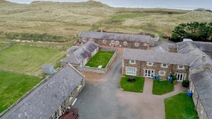 A stone building with multiple rooms, a paved driveway, and a grassy area in front. - 3 Bed in Alnwick (oc-80489) (Newton-by-the-Sea)