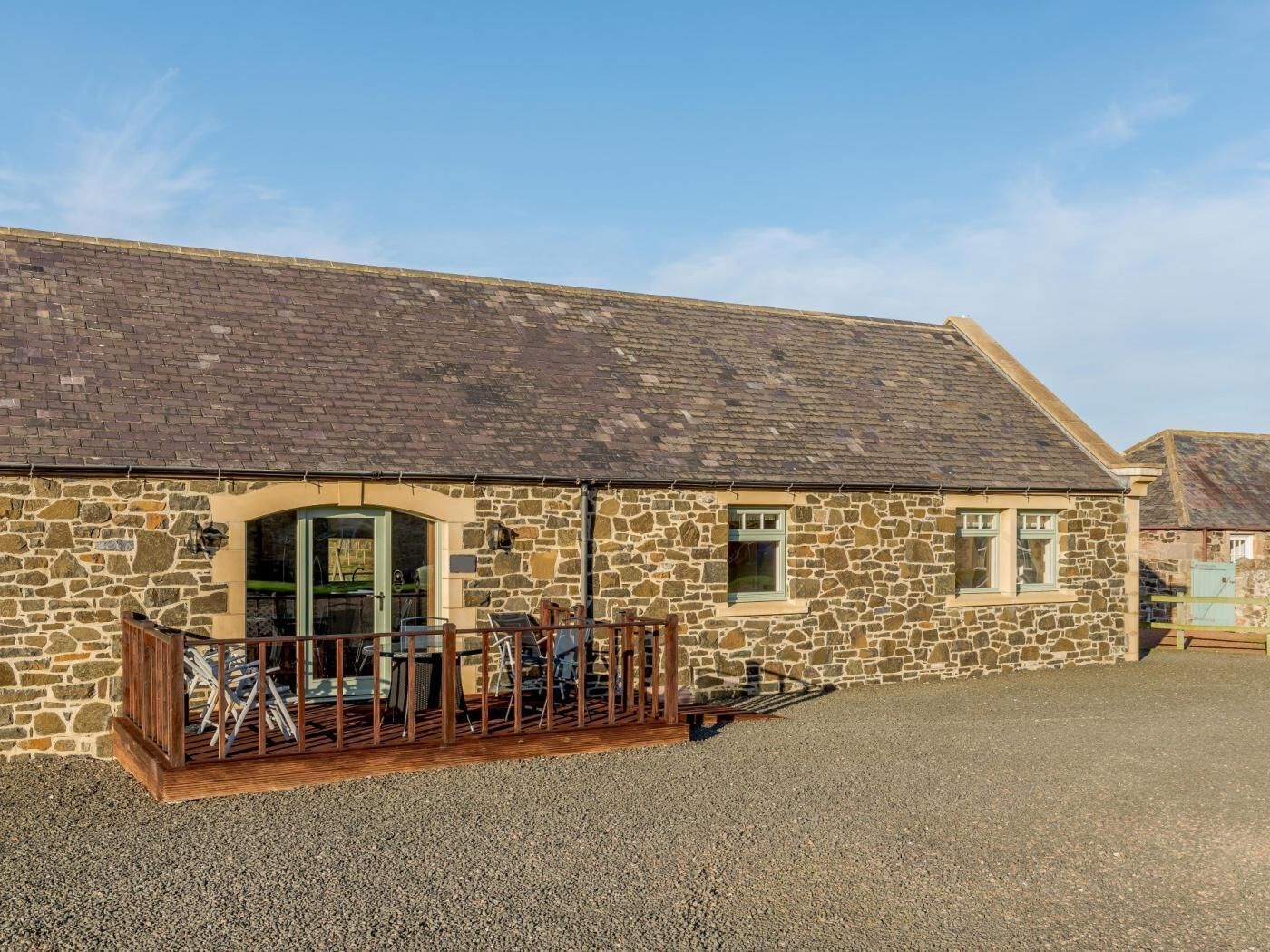 A stone building with a gravel driveway and a wooden fence.