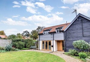 Ein zweistöckiges Haus mit geneigtem Dach, einer Holztür und einem kleinen Garten mit einer Bank.