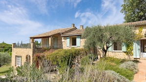 A stone house with a balcony, surrounded by a garden with various plants and a clear blue sky. - Peace and space in Vaison-la-Romaine for 16 people. (Saint-Romain-en-Viennois)