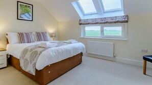 A bedroom with a large bed, a nightstand, a bedside table, a window with a view of the countryside, and a chandelier. - 2 Bed in Alnwick (oc-80499) (Newton-by-the-Sea)