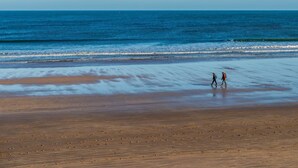 A beach with two people walking on the sand, a clear sky, and the ocean in the background. - 2 Bed in Alnwick (oc-80499) (Newton-by-the-Sea)