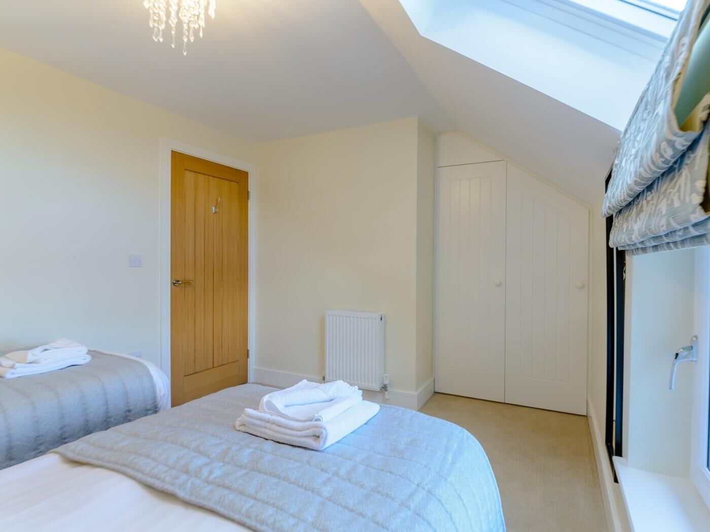 A bedroom with two beds, a wooden door, a radiator, and a window with curtains.