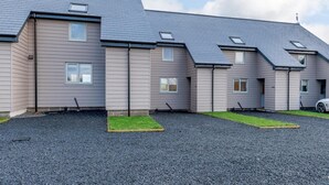 A row of modern, single-story houses with grey siding and dark roofs, featuring small windows and a gravel driveway. - 2 Bed in Alnwick (oc-80499) (Newton-by-the-Sea)