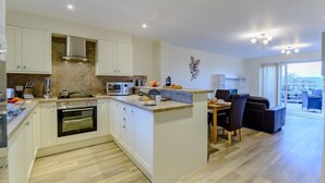 A modern kitchen with white cabinetry, a built-in oven, and a dining area with a table and chairs. - 2 Bed in Alnwick (oc-80499) (Newton-by-the-Sea)