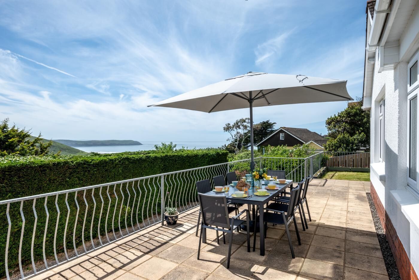 A patio with a table set for dining, overlooking a scenic view of the sea and hills.