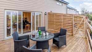 Une terrasse avec une table et des chaises en verre, une clôture en bois et une maison dotée de portes-fenêtres coulissantes.