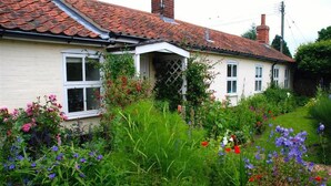 A traditional house with a tiled roof, a white exterior, and a garden with various flowers and plants. - 2 Bed in Snape (oc-sfoms) (Snape)
