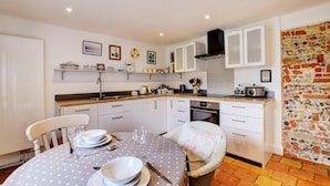 A compact kitchen with white cabinets, a built-in oven, and a stone wall. - 2 Bed in Snape (oc-sfoms) (Snape)