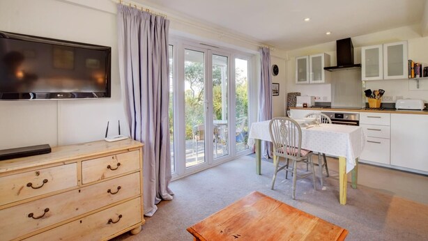 A modern kitchen with a dining area, a TV mounted on the wall, and a sliding glass door leading to a garden. - 2 Bed in Snape (oc-sfoms) (Snape)