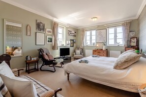 Ein Schlafzimmer mit einem großen Bett, einem Fernseher, einem Sessel, einer Kommode und Bildern an den Wänden.