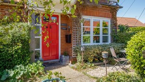 A brick house with a red door, a white window, and a garden with plants and a chair. - 1 Bed in Snape (oc-sfahs) (Snape)