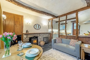 A cozy living room with a stone fireplace, wooden beams, a dining table set with plates and glasses, and a grey sofa with patterned cushions. - 2 Bed in Lindale (oc-c34128) (Lindale)