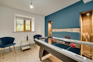 A room with a foosball table, two chairs, a small table with a bottle, and a window. - 3 Bed in Machynlleth (oc-bow321) (Glantwymyn)