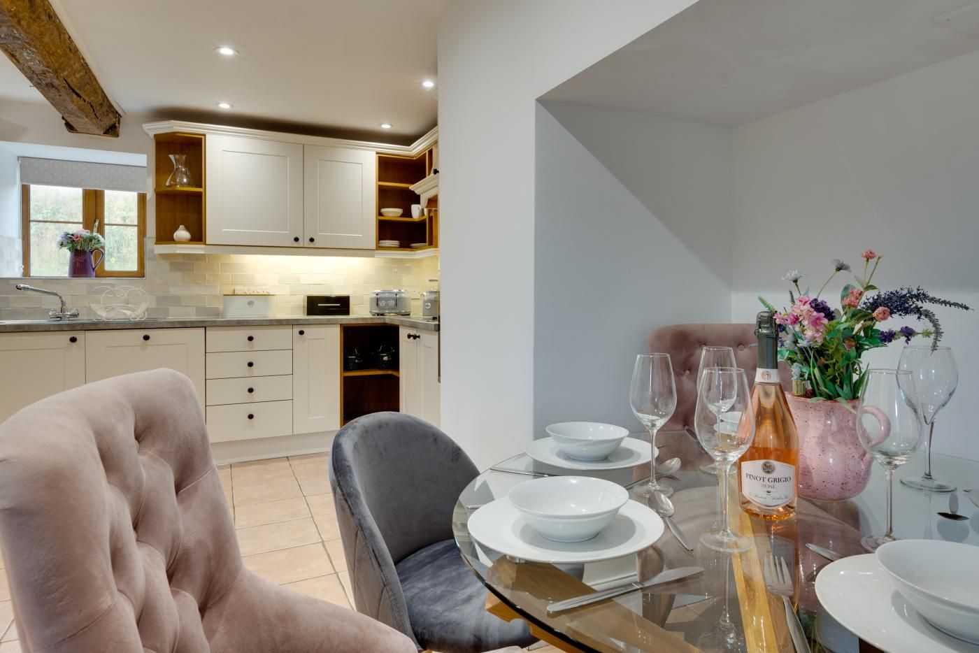 A dining area with a table set for two, a pink chair, and a vase with flowers.