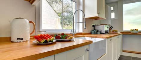 A kitchen with wooden countertops, white cabinets, a Breville kettle, and a fruit platter.